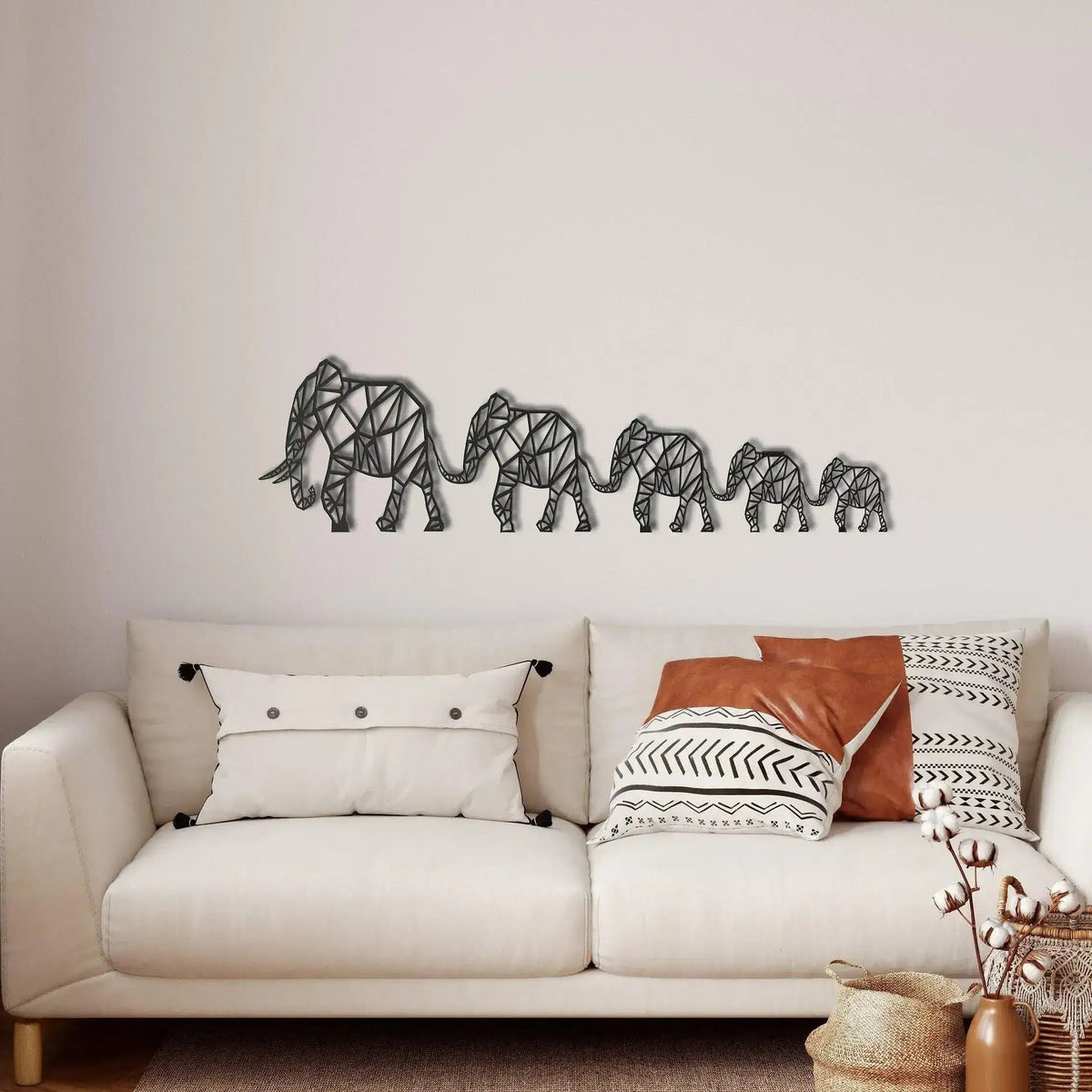 Geometric Elephant Family metal wall decor in dark finish on white wall — four polygon-style elephants walking in line above cream sofa