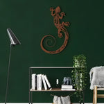 Bronze lizard metal wall decor with tribal cutout pattern on dark forest green wall above metal bookshelf