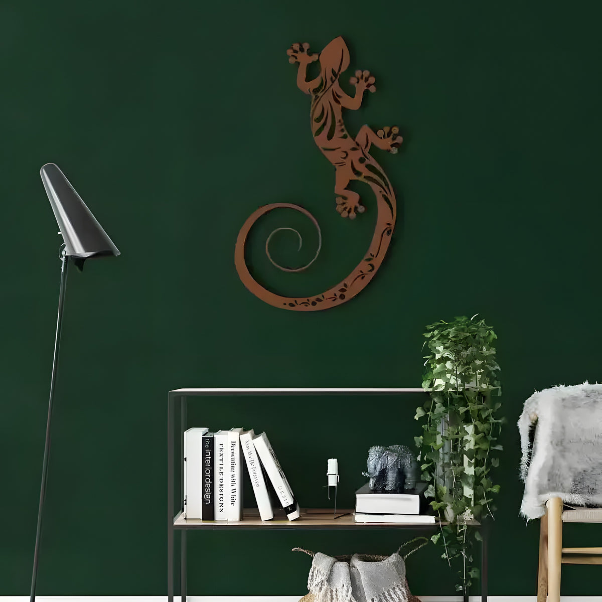Bronze lizard metal wall decor with tribal cutout pattern on dark forest green wall above metal bookshelf