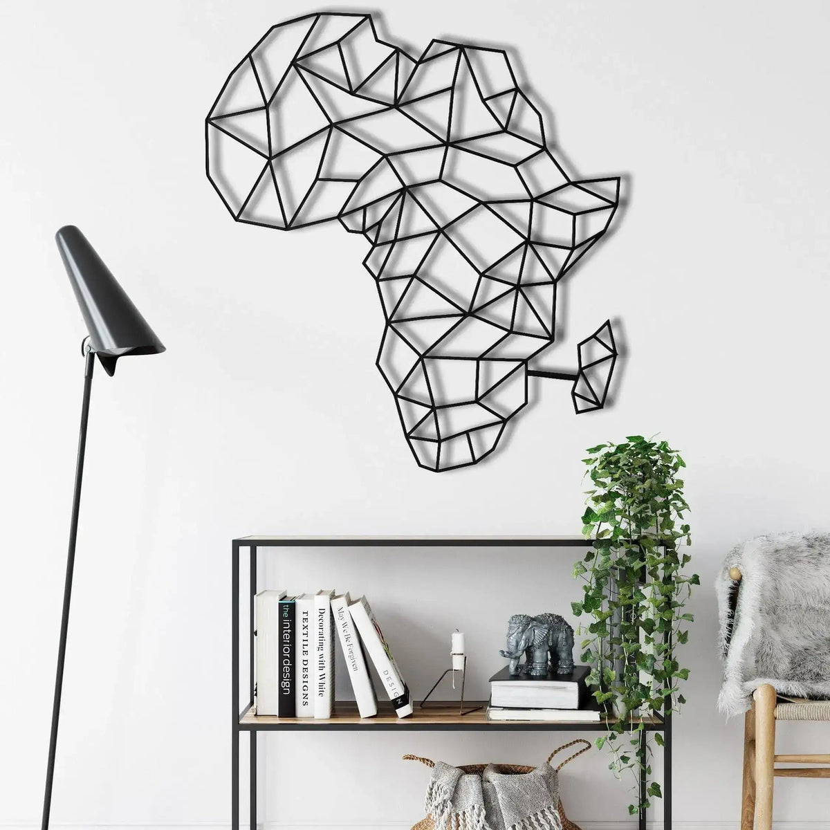 Black geometric Africa map wall decor on white wall above open-frame shelving, floor lamp and trailing ivy