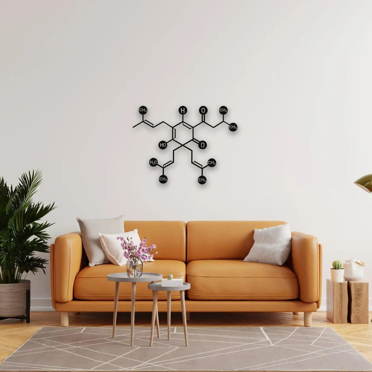Black beer molecule metal wall art with labeled chemical nodes on white wall above tan leather sofa and palm plant