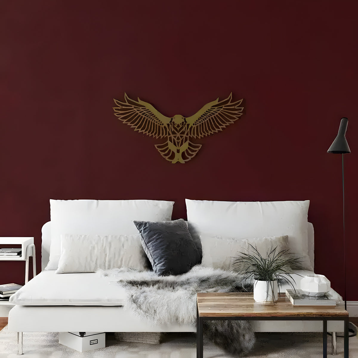 Gold geometric flying eagle with spread wings on dark burgundy wall above white sofa with fur throw