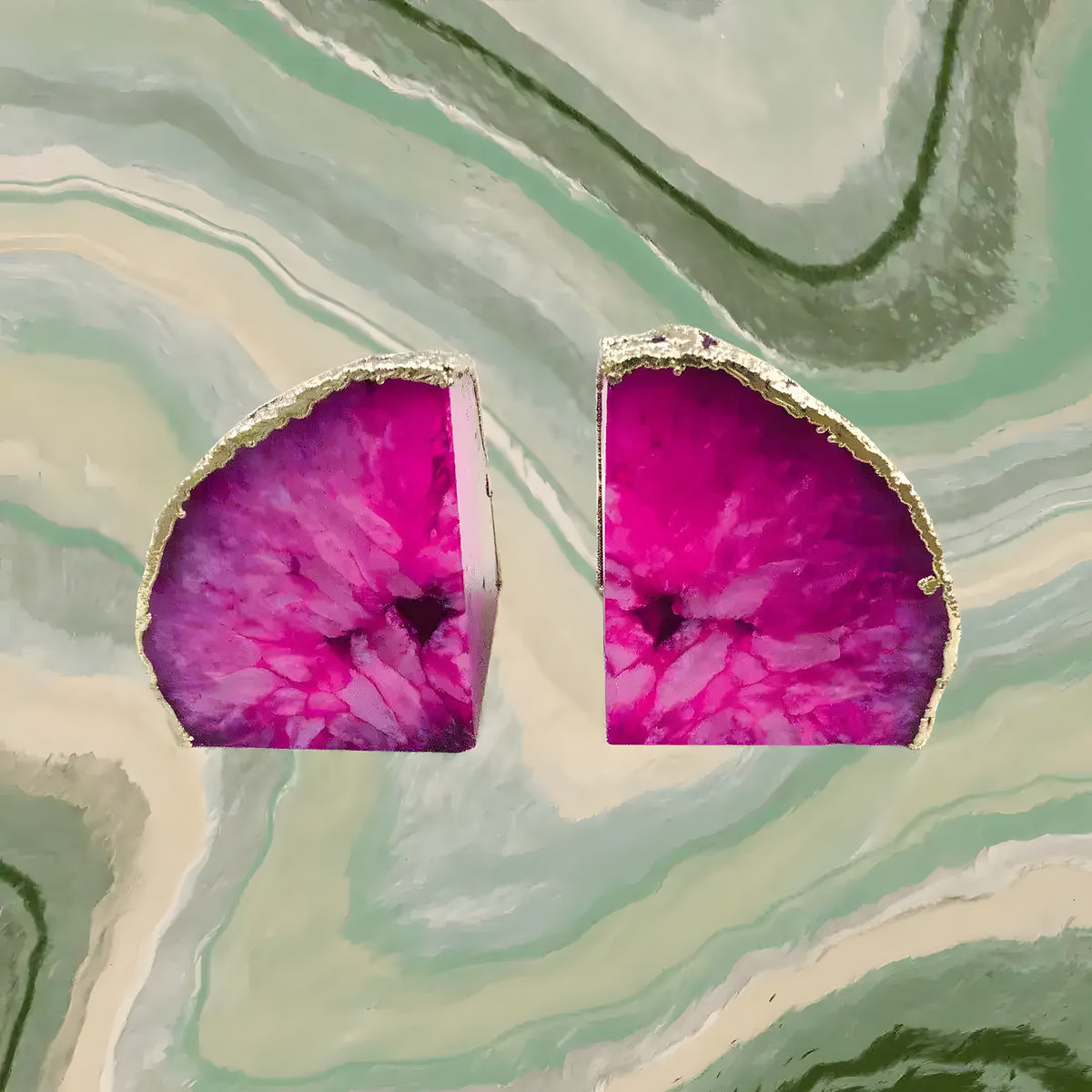 Pair of pink plated agate bookends, fuchsia geode slices with silver plated edges, top view on green marble background