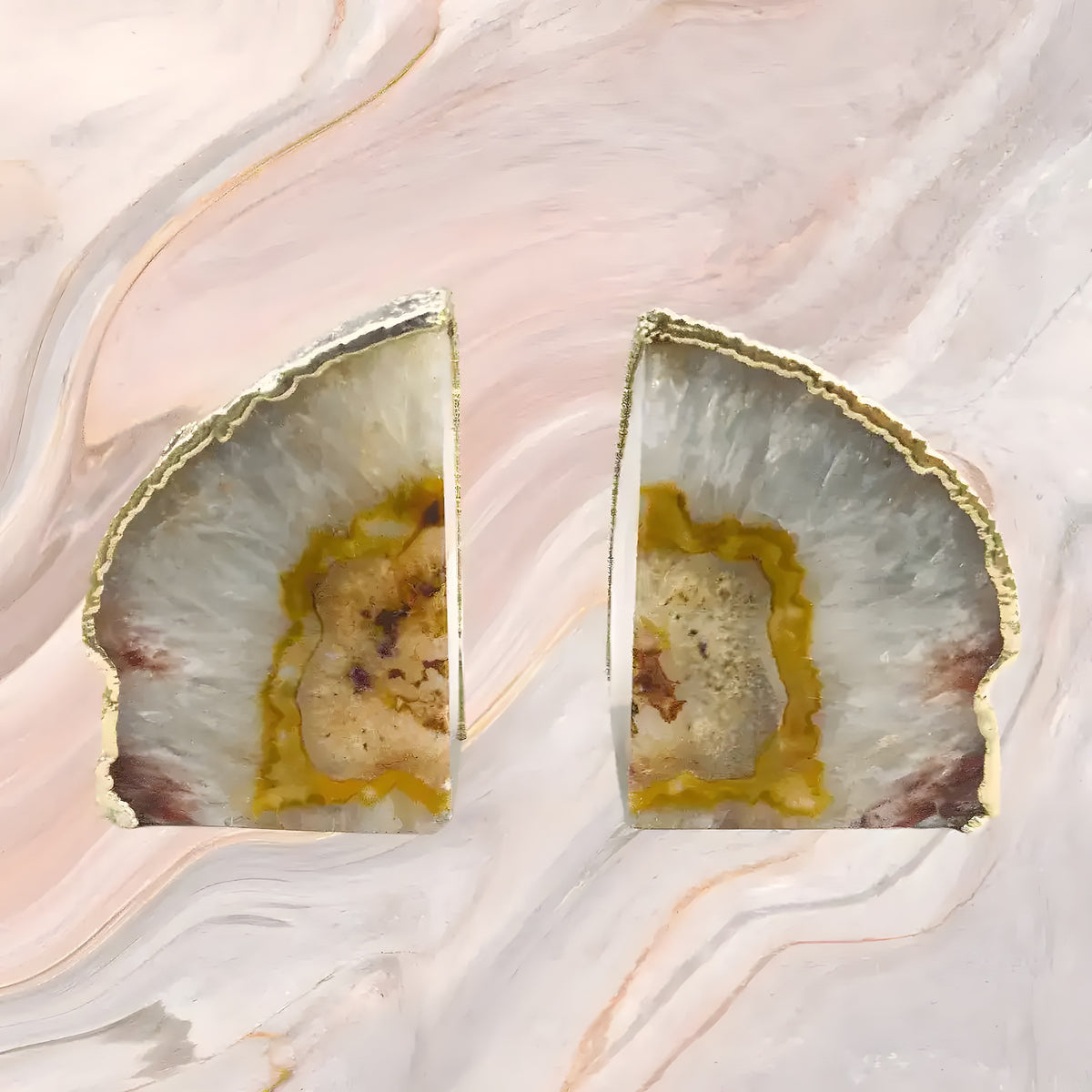 Pair of natural clear agate bookends with gold-plated edges on pink marble background