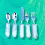 Set of 5 white agate cutlery on green marble background, pale blue translucent agate handles with silver spoons, knife, and forks