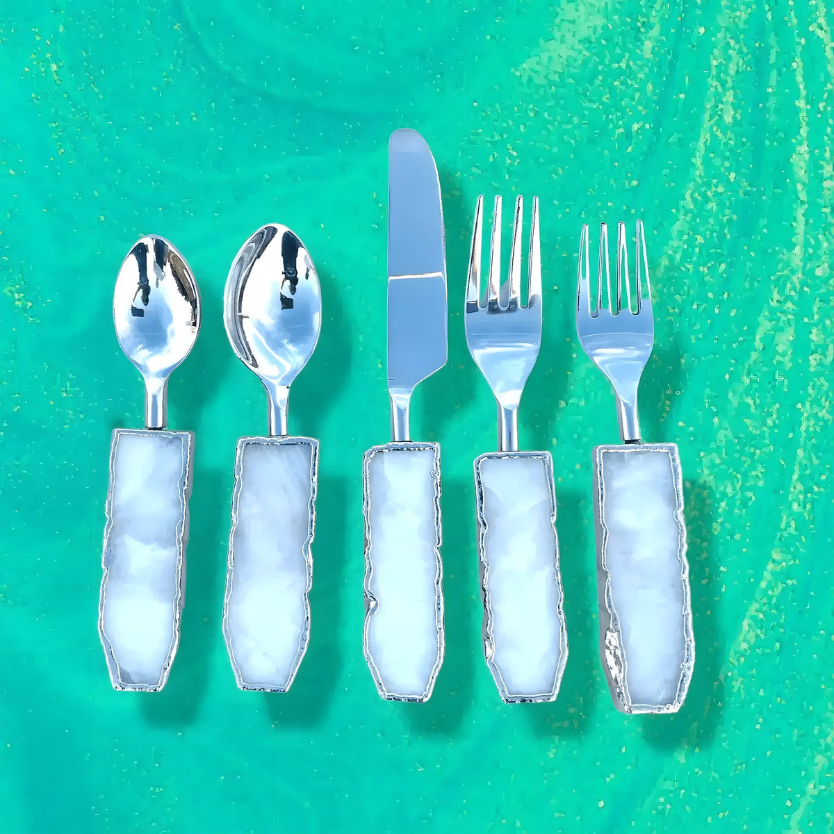 Set of 5 white agate cutlery on green marble background, pale blue translucent agate handles with silver spoons, knife, and forks