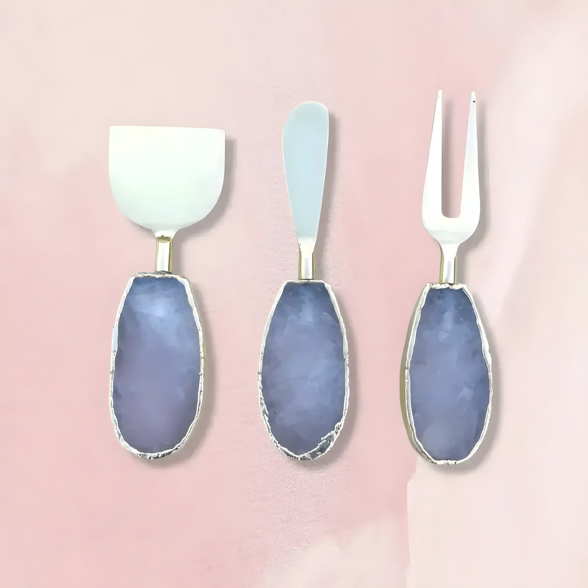 Set of 3 rose quartz cheese knives spreaders on pink background, white blades with oval lavender-blue stone handles and silver trim