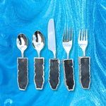 Five-piece labradorite agate cutlery set on blue marble: two spoons, knife, two forks with dark labradorite stone handles, silver trim