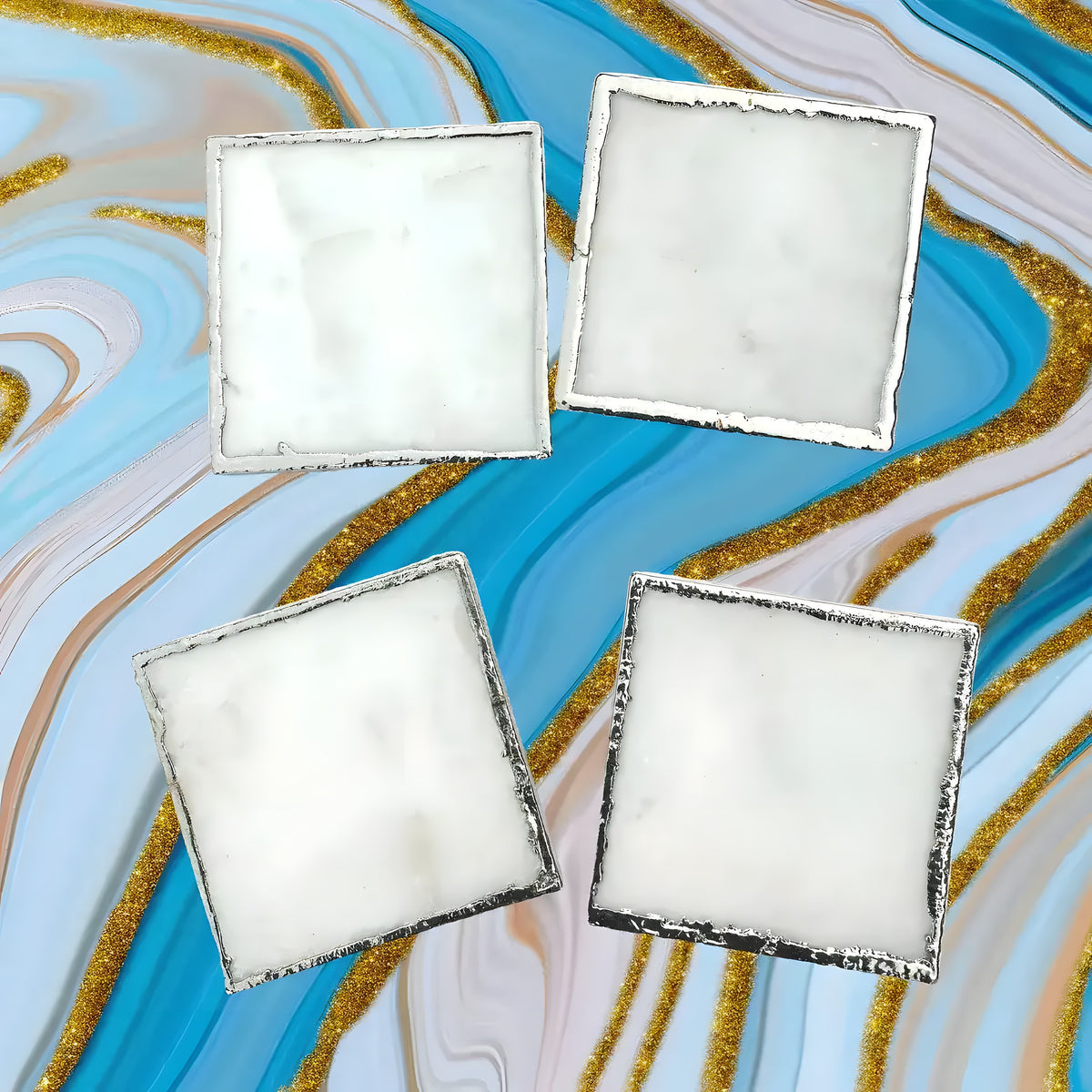 Set of 4 white marble plated coasters, square with silver-edged rims, arranged in two rows on blue and gold marble backdrop