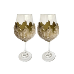 Two rose quartz wine glasses side by side, pale quartz crystal clusters wrapping bowl, jagged gold crown rim, clear stem and base