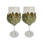 Two wine glasses with clustered light green quartz chips encrusting bowl, gold scalloped crown rim, on grey background