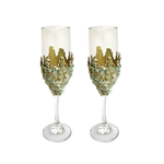 Two tall champagne flutes adorned with light green quartz chips clustered around the lower bowl, topped with gold crown-like embellishment