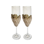 Two tall rose quartz champagne flutes with blush chip-encrusted bowl and gold wave crown rim, clear stem and base on white