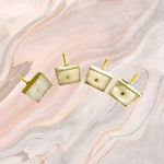 Four square white agate drawer pulls with gold frames and posts on pink marble background