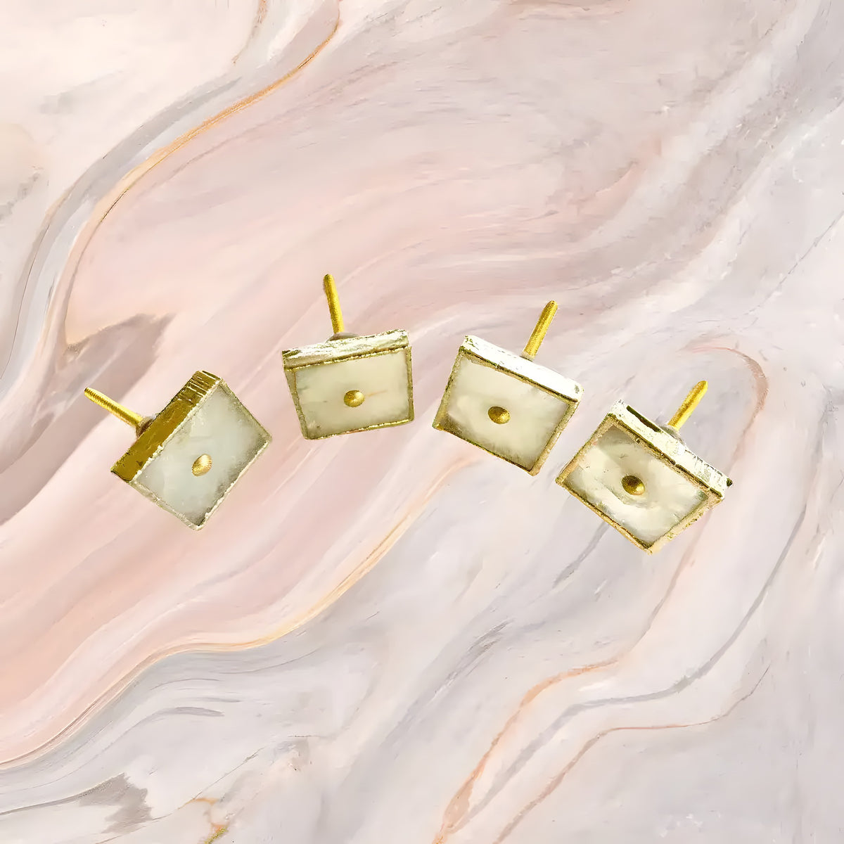 Four square white agate drawer pulls with gold frames and posts on pink marble background