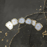Six white agate cabinet pull handles in curved row on dark marble, organic shapes, gold hammered edges, single gold dome stud each