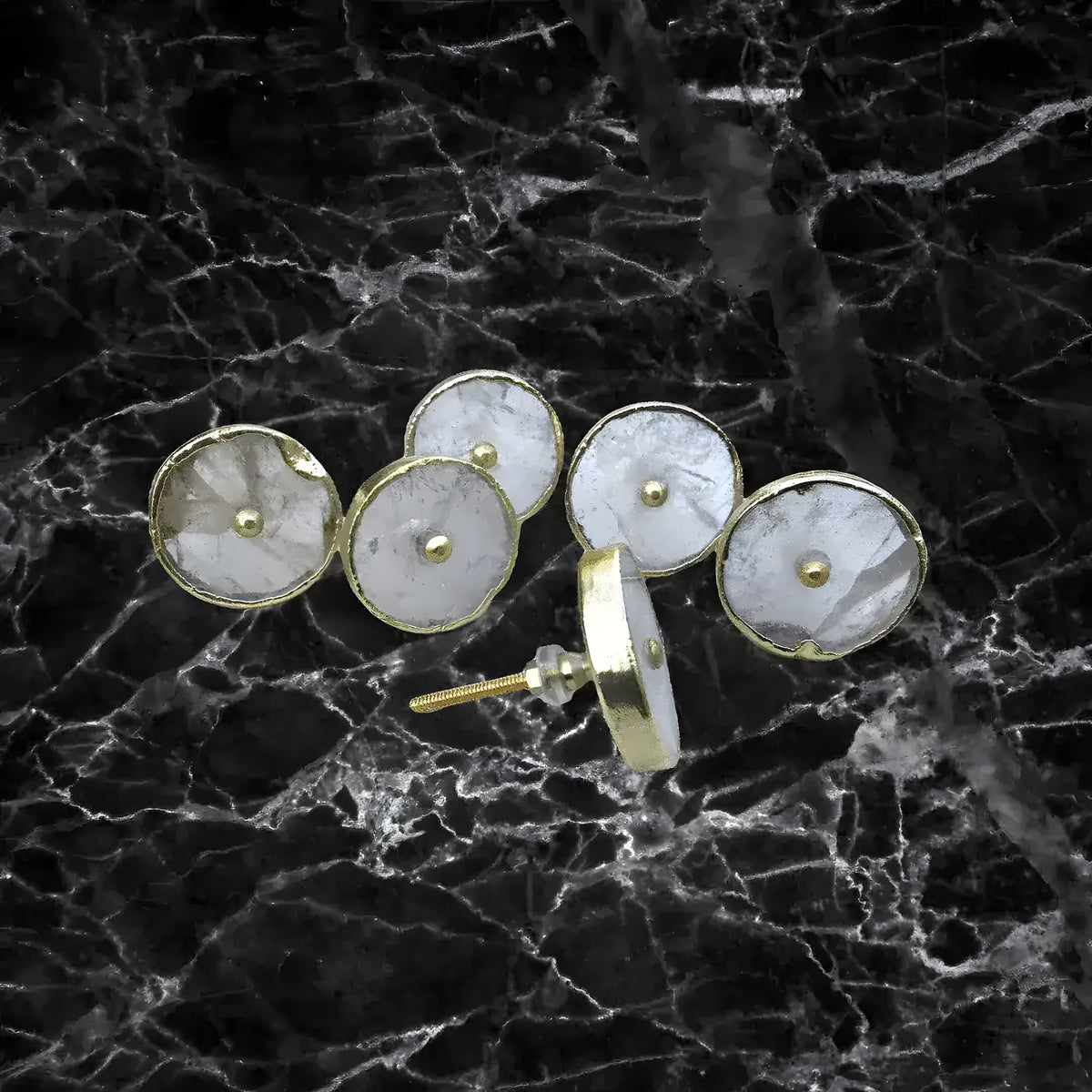 Six round clear quartz cabinet knobs with gold bezels on black marble surface, one showing screw post hardware