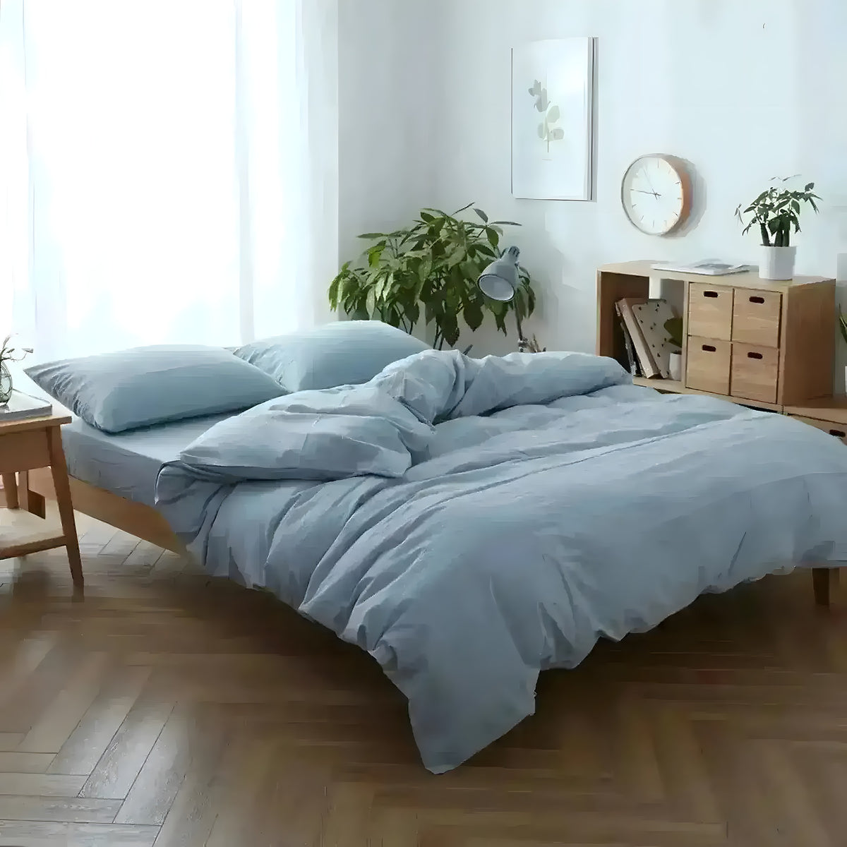 Sky blue cotton duvet cover set in Scandinavian bedroom, powder-blue duvet and matching pillows on low wooden platform bed, plants and shelving
