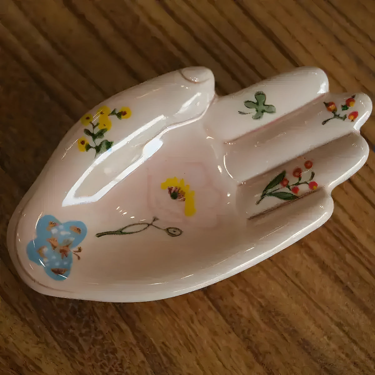Glazed porcelain hand sculpture trinket dish with floral botanical prints lying flat on wooden surface