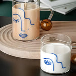 Two female face water glasses — large with latte and small with milk — clear glass with blue line-art face