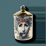 White ceramic flower Lina Cavalieri candle jar with polished gold domed lid, decorated with woman's face surrounded by blue and pink roses