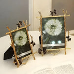 Two gold brass butterfly photo frames with twig-and-butterfly borders displayed together on a surface