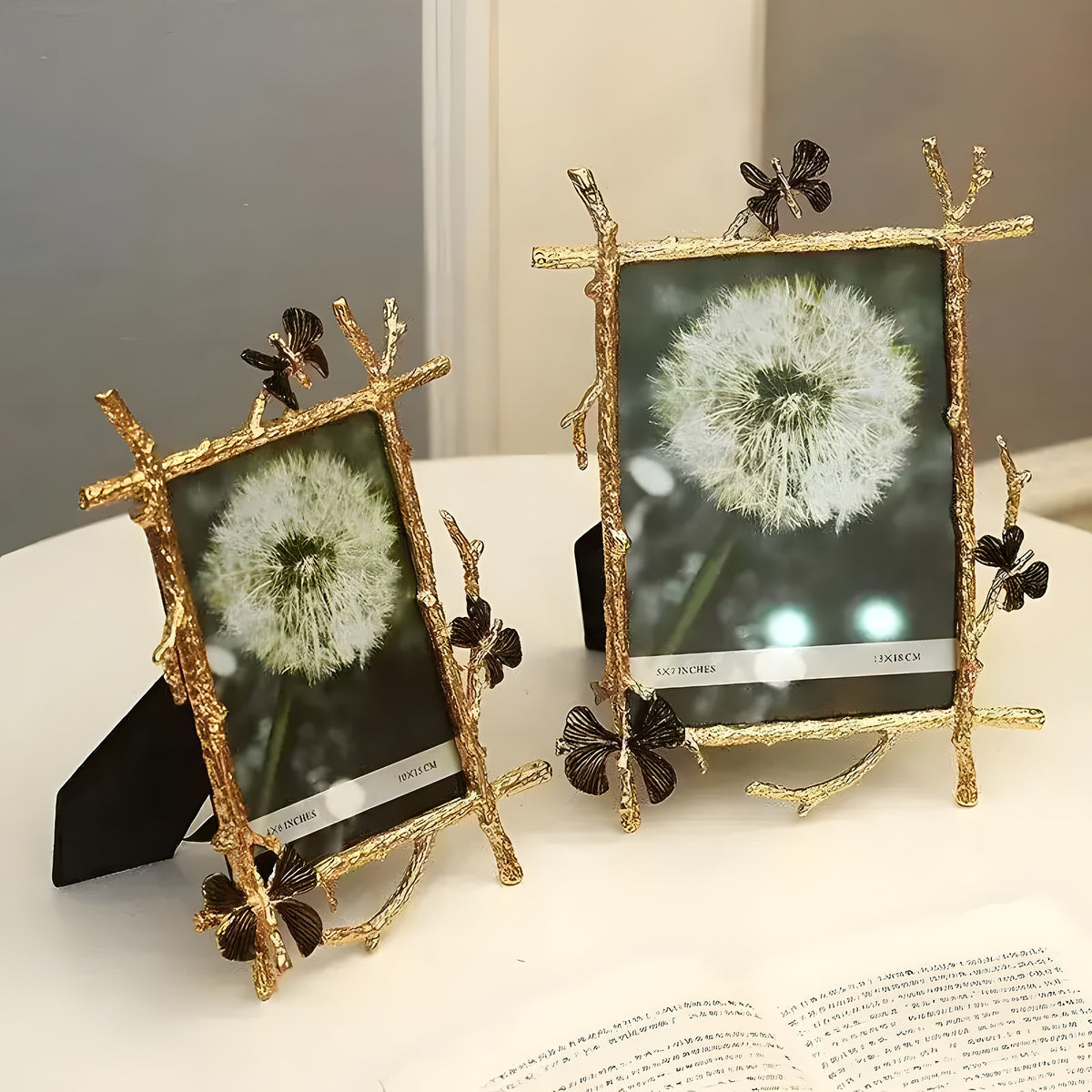 Two gold brass butterfly photo frames with twig-and-butterfly borders displayed together on a surface