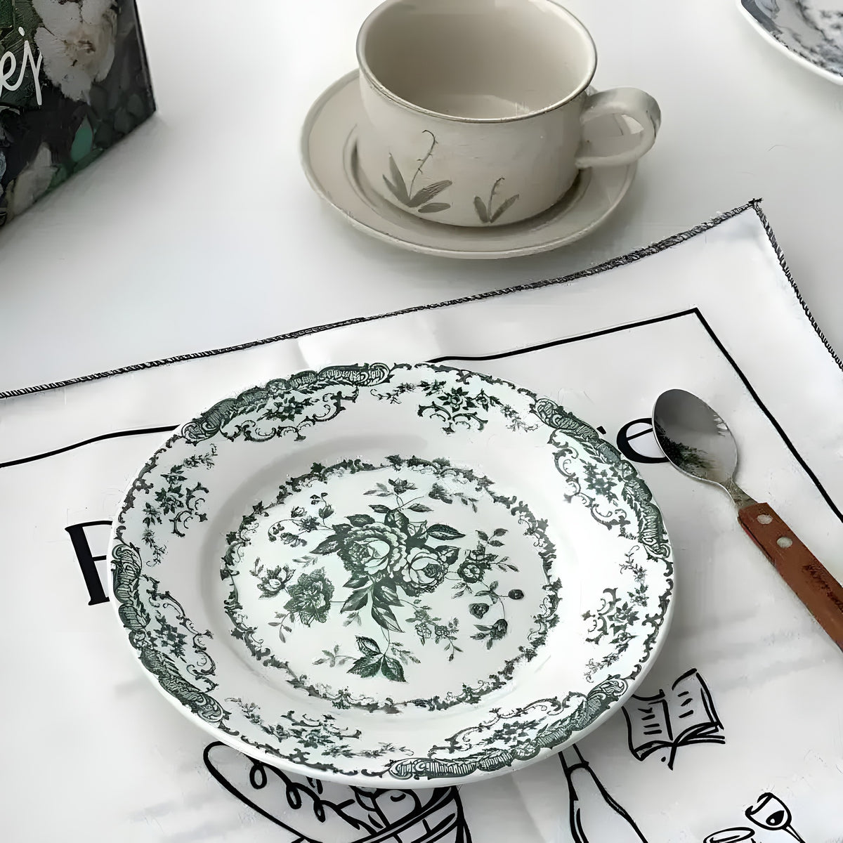 Rose dessert plate with dark green floral print, ornate scalloped border, styled at table with teacup