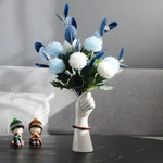 White ceramic hand-shaped vase with bracelet holding blue white pom-pom flowers, marble table