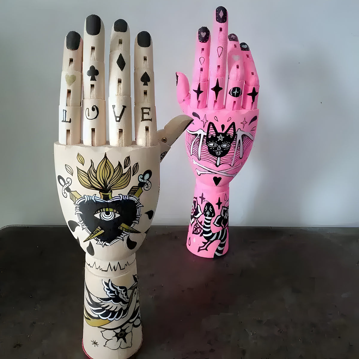 Pair of cream and pink tattooed wooden movable joint hand decor with mystic symbols and cat art, dark background