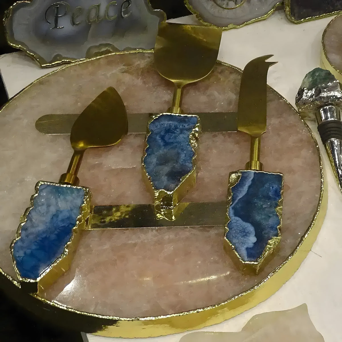 Blue agate brass cheese knife set — three knives with agate handles and gold blades on rose quartz tray