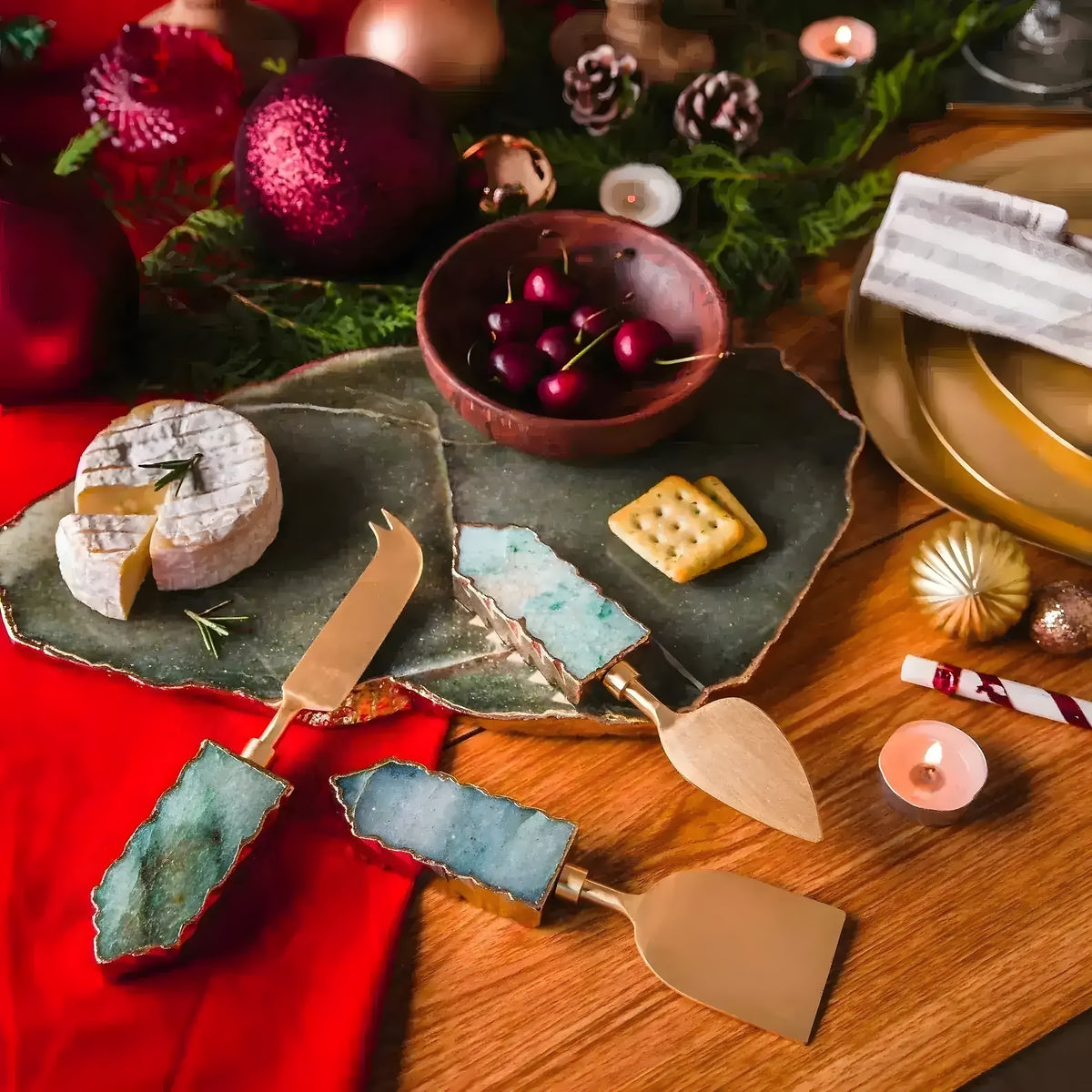 Three green aventurine cheese knives with gold handles styled on slate board with camembert and holiday ornaments