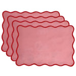 Set of four pink cotton rectangular placemats with red wavy scallop border, stacked in fanned arrangement