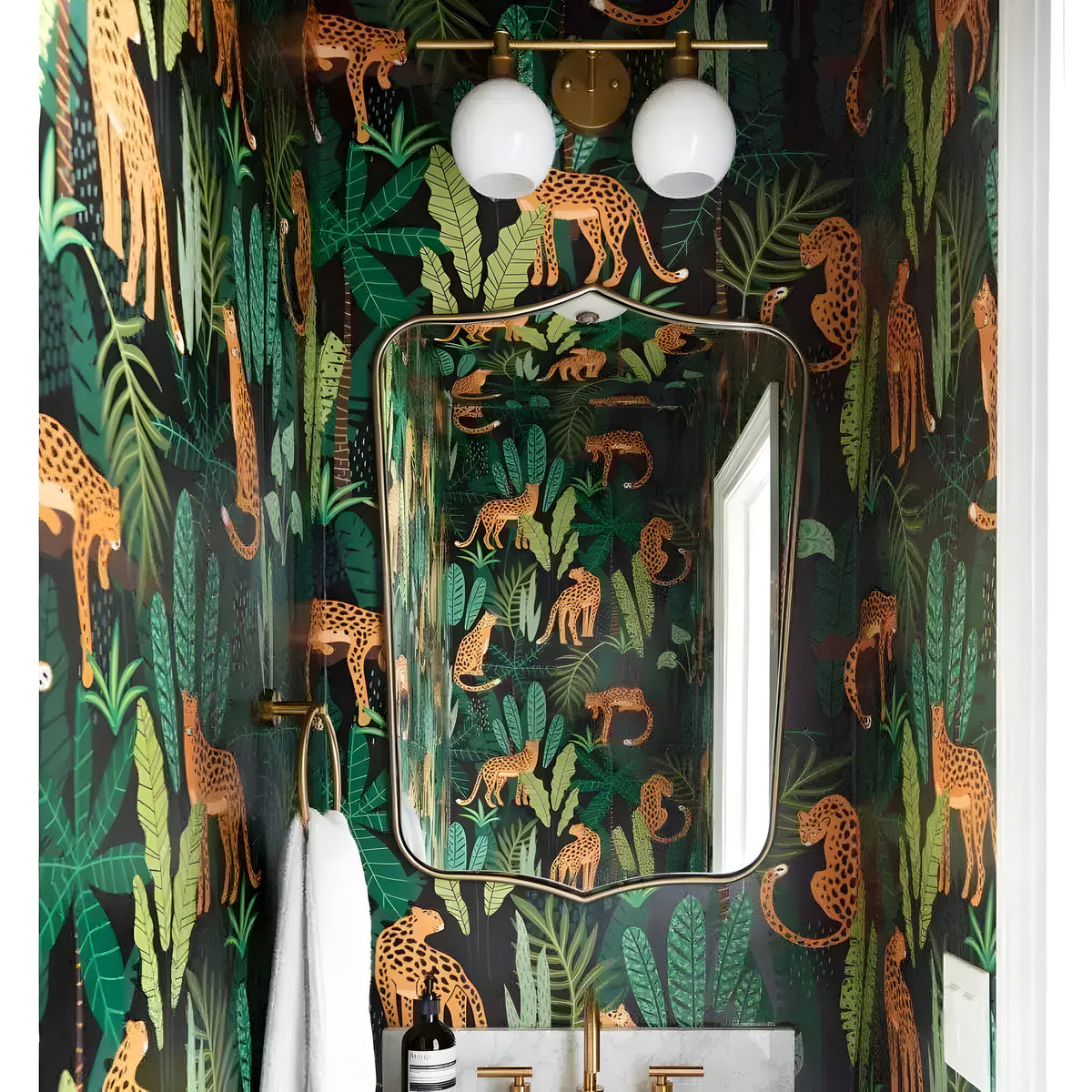 Custom wallpaper dark jungle print with golden cheetahs and tropical leaves in bathroom with brass fixtures and globe lights