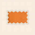 Single orange linen scallop placemat on cream background, rectangular with wavy white scallop border, flat lay