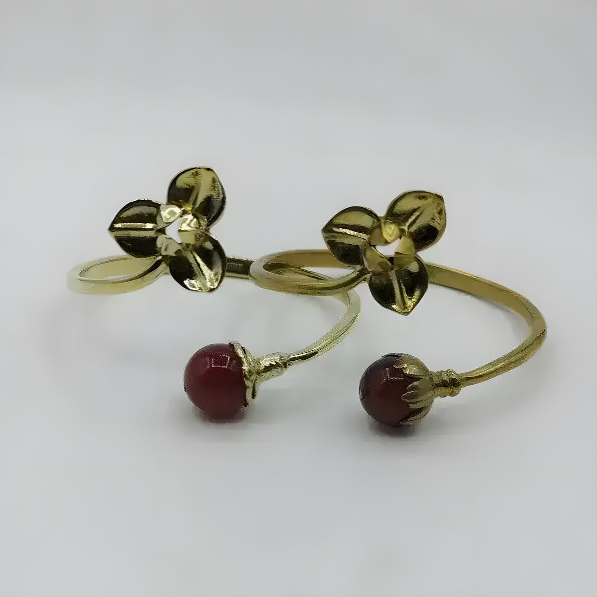 Two pearl-style brass flower bangles with gold flower charm at top and deep red bead tip, open-cuff design on white background