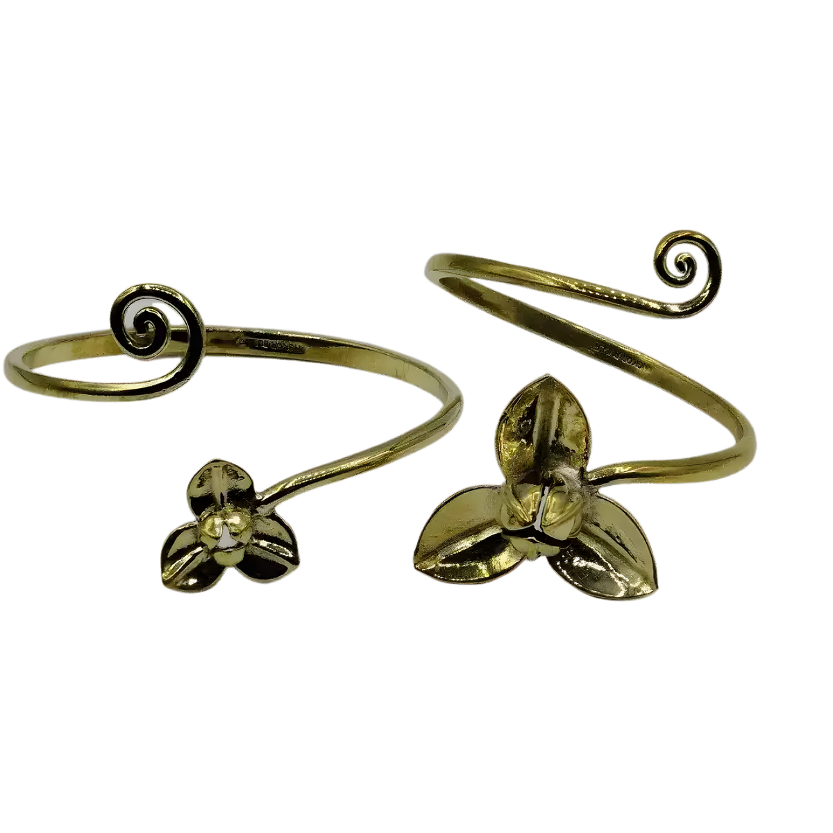 Two swirly brass flower bangles on white background, open-cuff style with curled swirl tips and three-petal flower charms