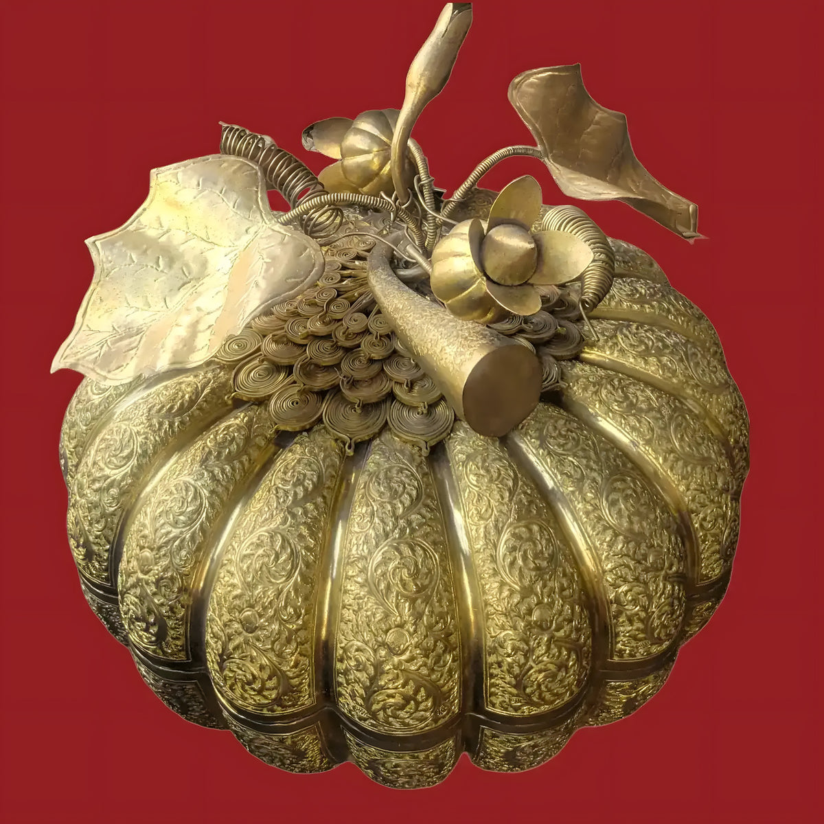 Cambodian engraved brass pumpkin betel box, gold, intricate floral scrollwork, decorative stem and leaves, against red