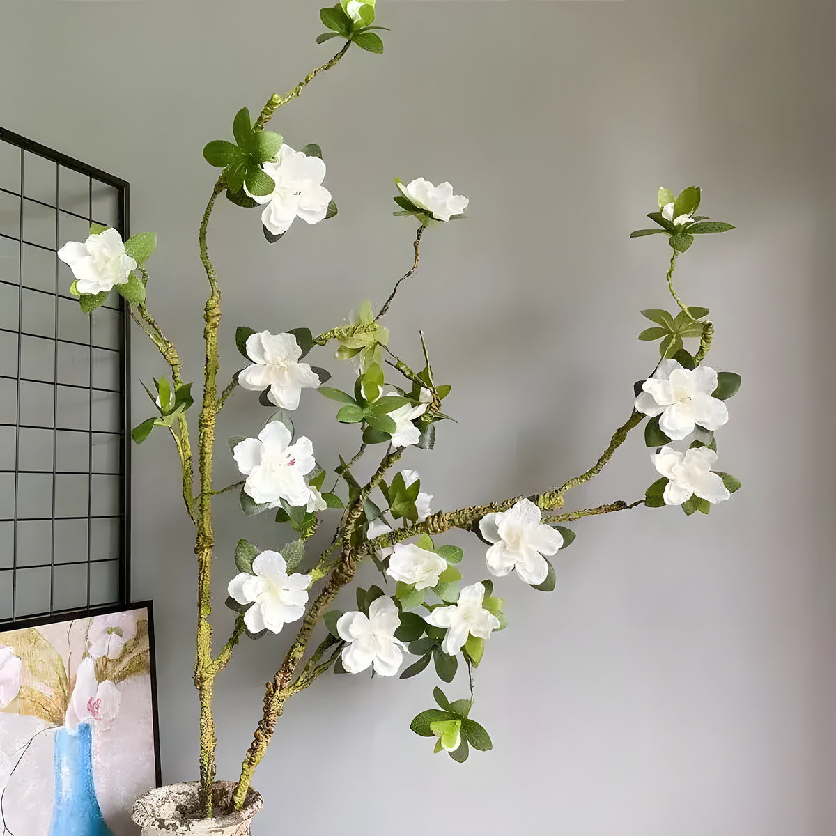 Extra-large white azalea flower branch in rustic vase, white blooms with green leaves on textured brown branch against grey wall