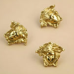Three polished gold brass angel face cabinet pulls on beige surface showing sculptural curly hair detail