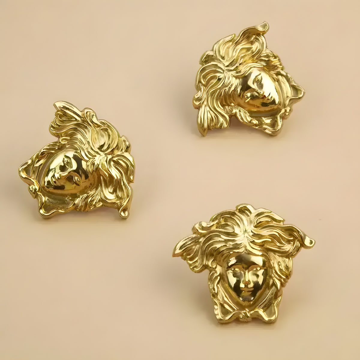 Three polished gold brass angel face cabinet pulls on beige surface showing sculptural curly hair detail