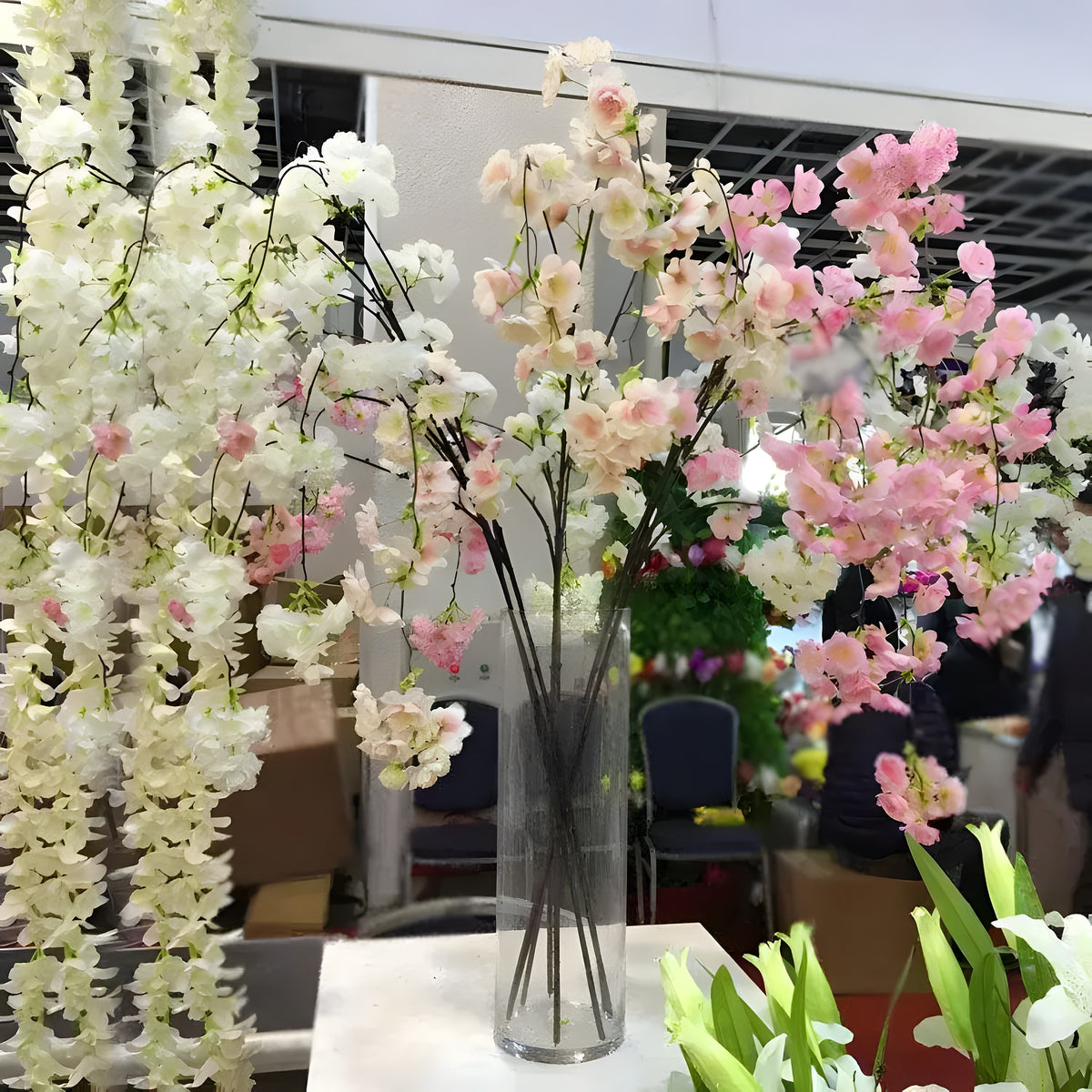 Extra-large cherry blossom branches in pink and white displayed in a glass cylinder vase, trade show setting