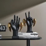 Two golden wings victory hand figurines — matte black hands making peace signs, gold angel wings, styled on books