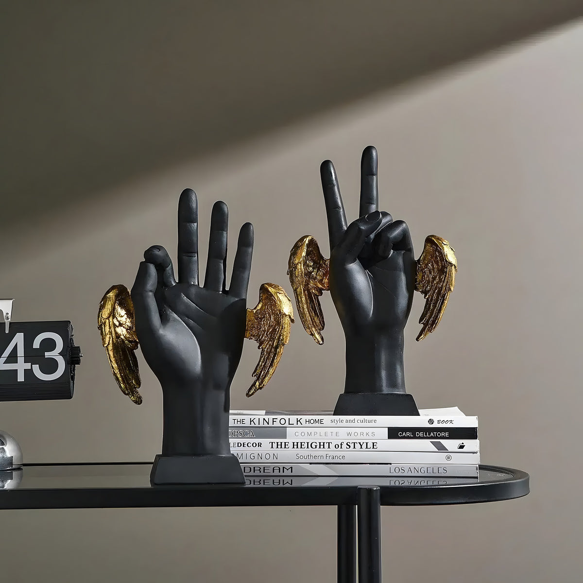Two golden wings victory hand figurines — matte black hands making peace signs, gold angel wings, styled on books