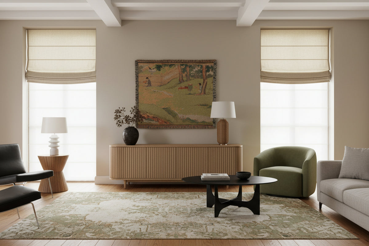 A rectangular woven throw blanket featuring a vintage-style landscape scene with figures, trees, and a grassy field, finished with fringed edges.