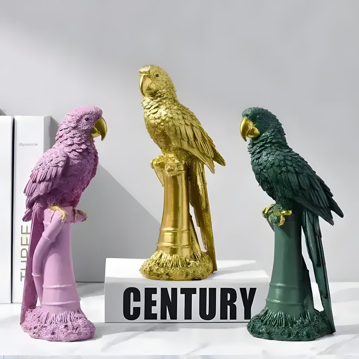 Three exotic parrot figurines in pink, gold, and dark green on cylindrical perch stands, marble surface