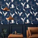 Navy wallpaper with white flying cranes above panelling with copper pendant lamps and tan leather seat