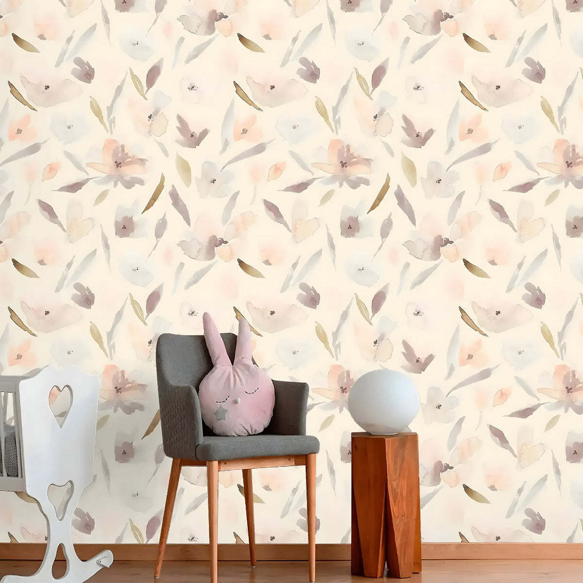 Nursery with grey chair and crib against pastel watercolor blossom wallpaper on cream
