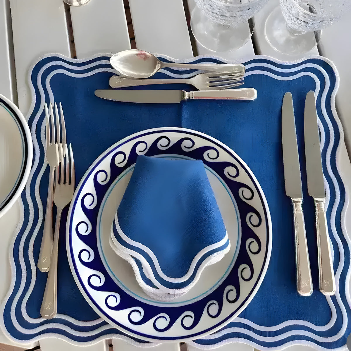 royal blue Marin Wave placemat with white wavy scalloped border, set with matching wave plate and folded napkin