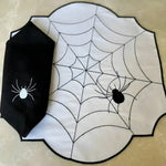 Spiderweb placemat flat lay, white shaped mat with black embroidered web and spider, black napkin with white spider embroidery